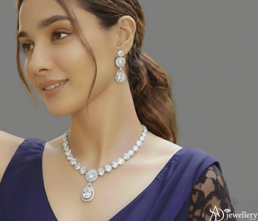 Rhodium-plated CZ halo and teardrop bridal necklace set displayed on a woman wearing a deep blue dress, featuring a matching teardrop pendant necklace and coordinating drop earrings