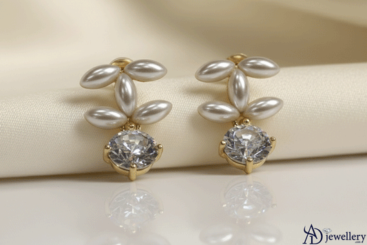 A pair of elegant Diamond Snowburst Drop Earrings featuring marquise-shaped pearls arranged in a floral design above a round brilliant-cut diamond set in gold, displayed on a soft cream fabric background